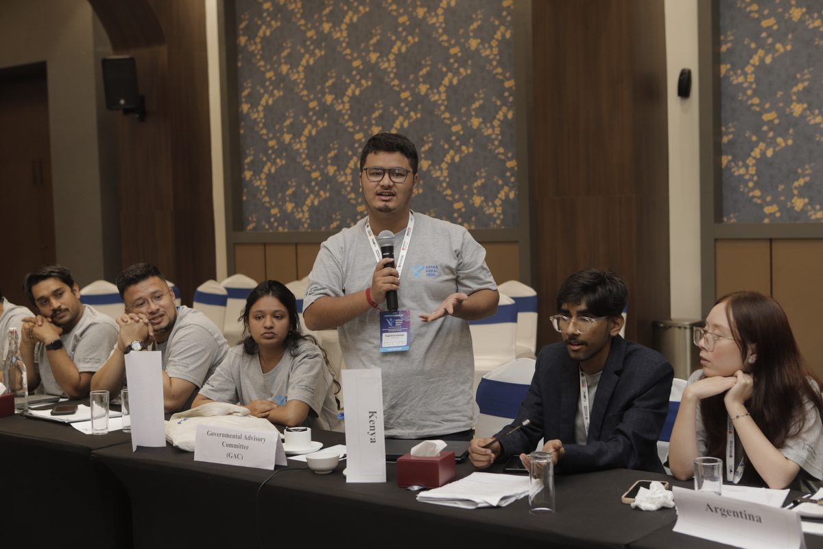 Suprince Kasaju speaking at APIGA Nepal 2026, seated with the Governmental Advisory Committee delegation